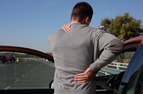 A man getting out of a car after a rear-end accident in Montgomery with his hands on his back, indicating an injury to his spine was caused.