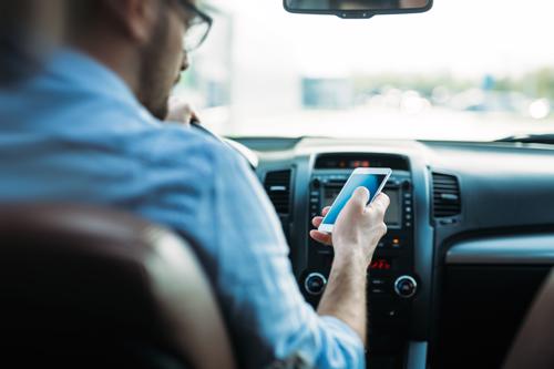 A man using his cell phone while driving, taking his attention off the road and increasing his chances of causing and accident.