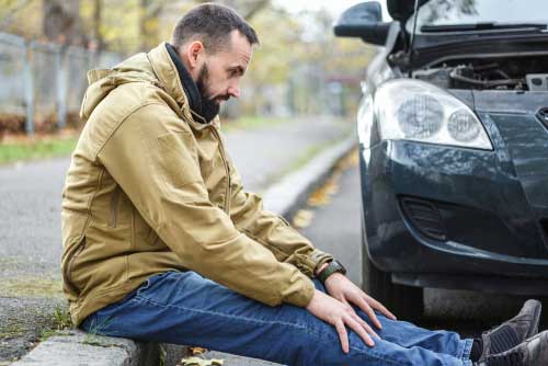 A man sitting on the side of the curb after experiencing a car accident.