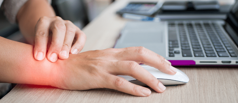 Image of someone touching a sore wrist while typing at a computer